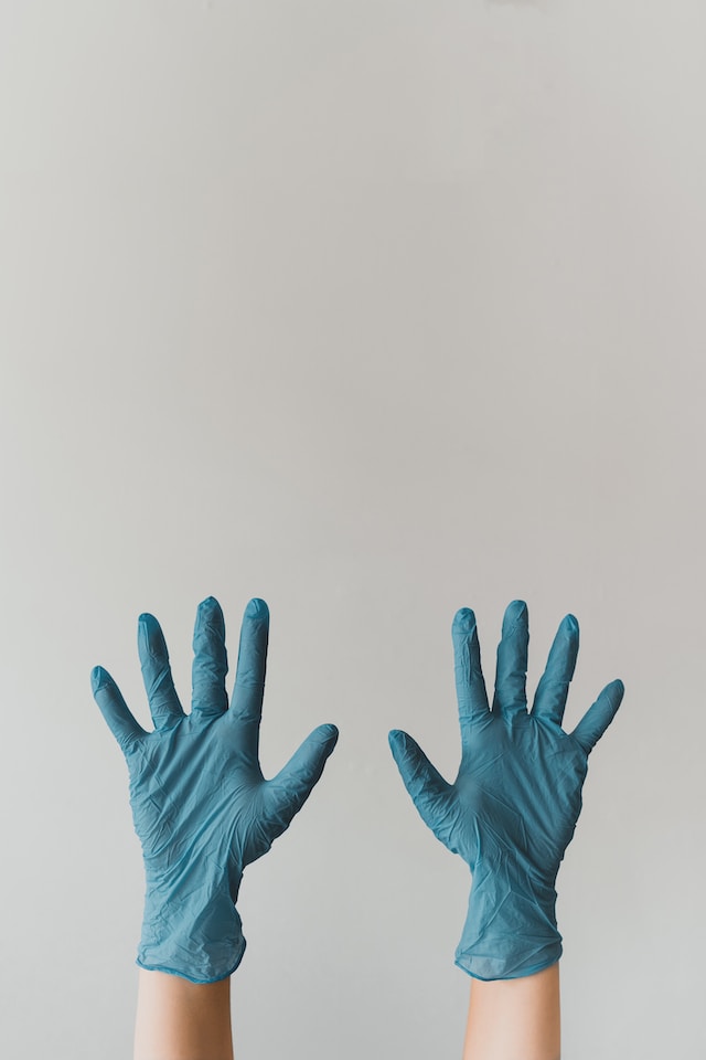 A person holding their hands up wearing blue gloves, an essential part of cleaning up after mice